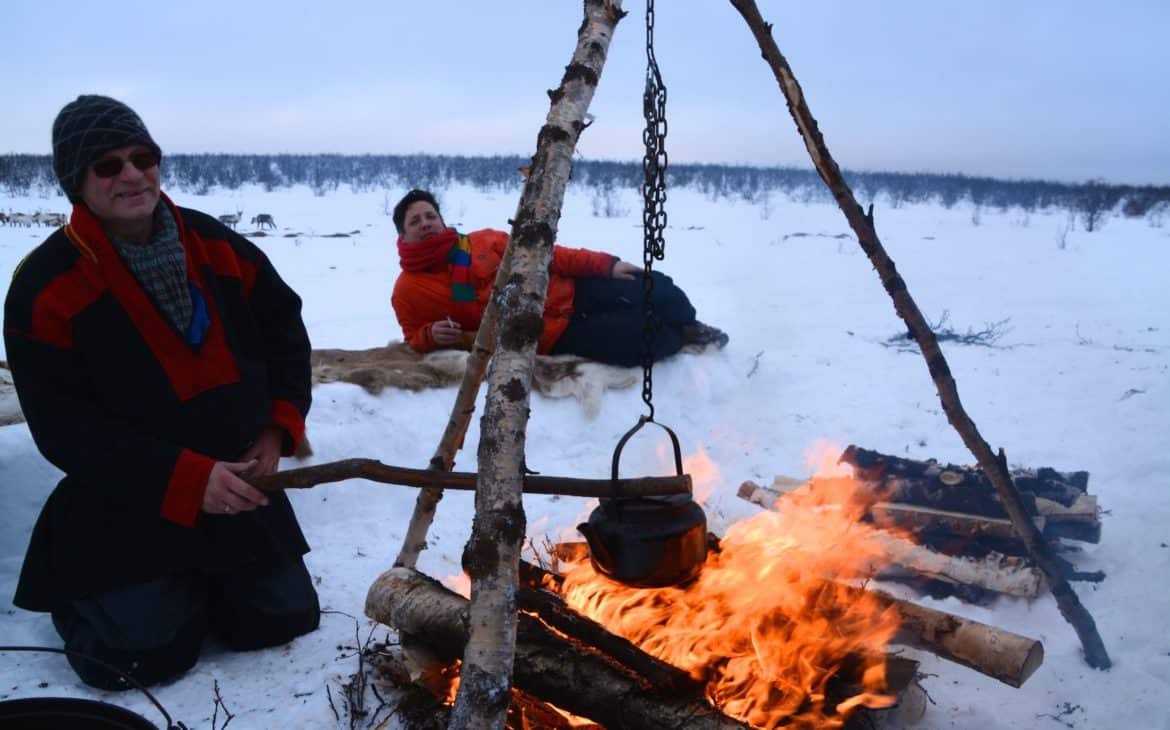 Mann erheizt Suppe über Lagerfeuer in verschneiter Landschaft