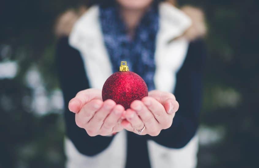 Frau hält rote Weihnachtskugel in Händen