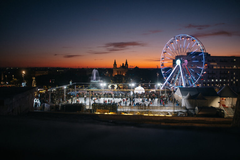 Blick auf die Eislaufbahn, das Riesenrad und die Hütten des Weihnachtsmarkts in Malta bei Nacht mit festlicher Beleuchtung.