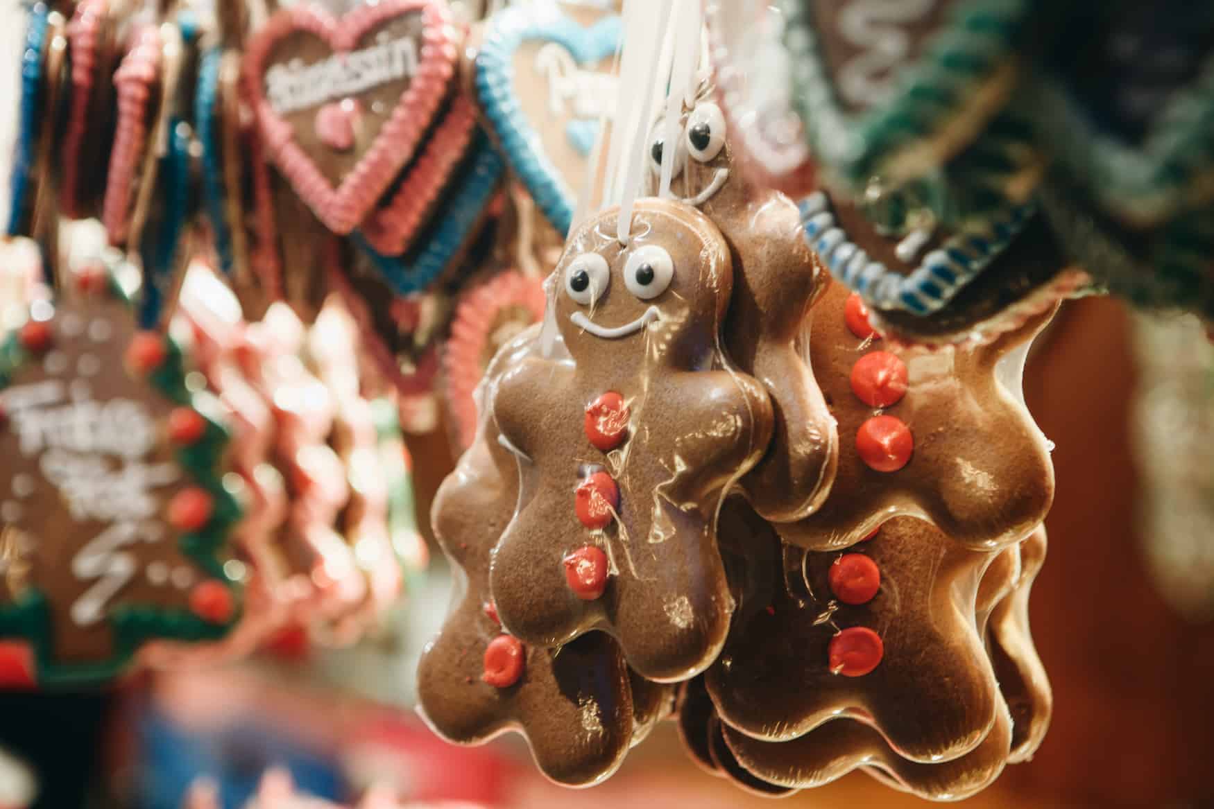 Vor guten Lebkuchenherzen hängen Lebkuchenmänner mit roten Zuckerperlen auf dem Körper an einem Stand auf dem Weihnachtsmarkt.