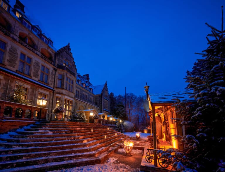 In der Dunkelheit sind die verschneiten Treppen und das Schloss Kronberg festlich erleuchtet. Gegenüber vom Eingang in das Schloss steht eine einladend beleuchtete Weihnachtsmarkthütte.