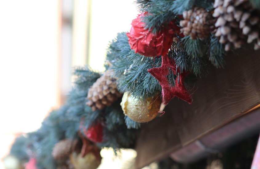 Das Dach von einem Stand auf dem Weihnachtsmarkt ist mit Tannenzweigen, -zapfen und Schmuck aus rot und gold dekoriert.