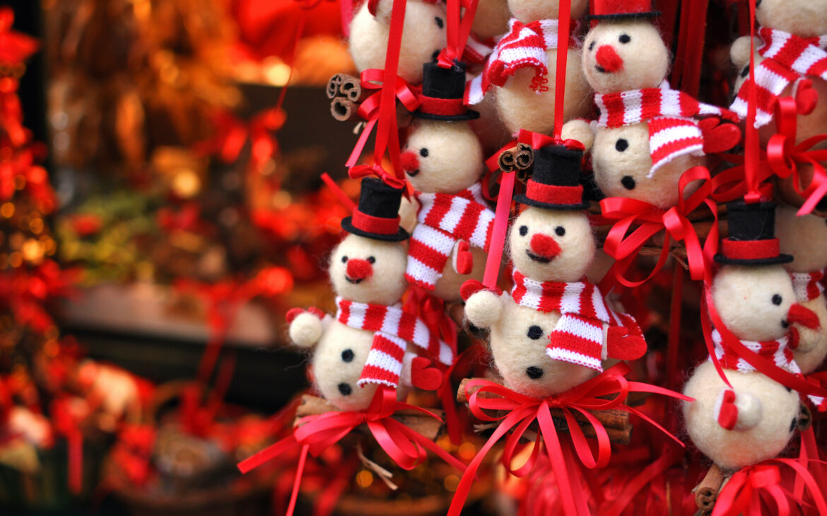 Kleine Schneemänner mit roter Nase, Hut und rot-weißem Schal and roten Scheiben hängen zum Verkauf in einem Stand auf dem Weihnachtsmarkt.