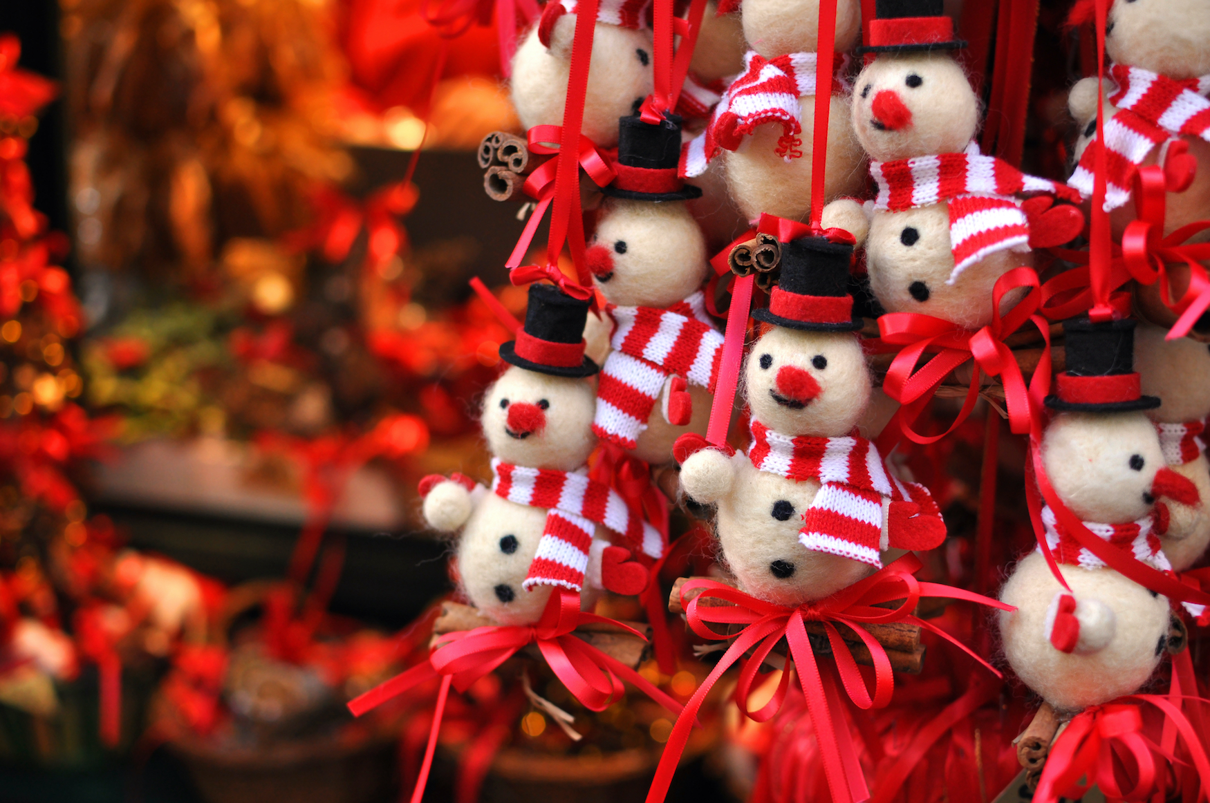 Kleine Schneemänner mit roter Nase, Hut und rot-weißem Schal and roten Scheiben hängen zum Verkauf in einem Stand auf dem Weihnachtsmarkt.