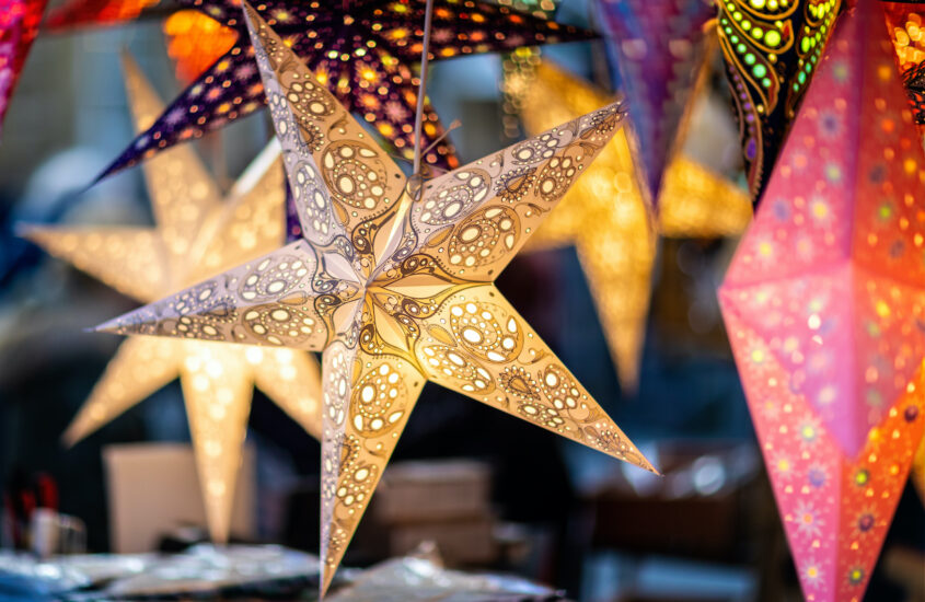 Ein großer beleuchteter Weihnachtsstern hängt mit anderen roten und bunten Sternen in einem Stand auf dem Weihnachtsmarkt.