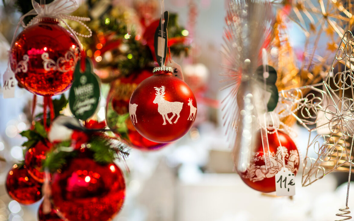 Rote Christbaumkugeln und glitzernder Christbaumschmuck hängen in einem Stand auf dem Weihnachtsmarkt.