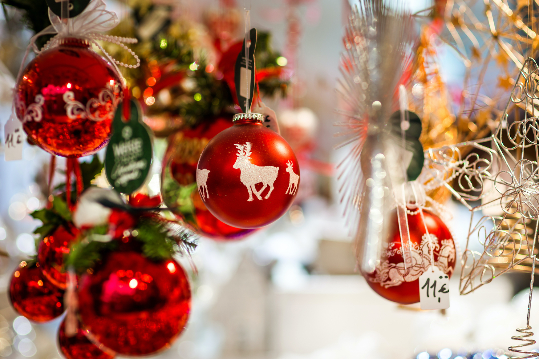 Rote Christbaumkugeln und glitzernder Christbaumschmuck hängen in einem Stand auf dem Weihnachtsmarkt.