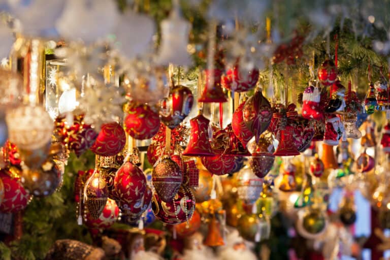 Christbaumkugeln und -glocken in dunklem rot mit goldenen Verzierungen hängen in einem Stand auf dem Weihnachtsmarkt.