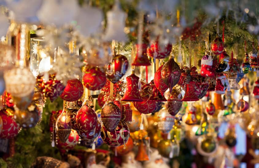 Christbaumkugeln und -glocken in dunklem rot mit goldenen Verzierungen hängen in einem Stand auf dem Weihnachtsmarkt.