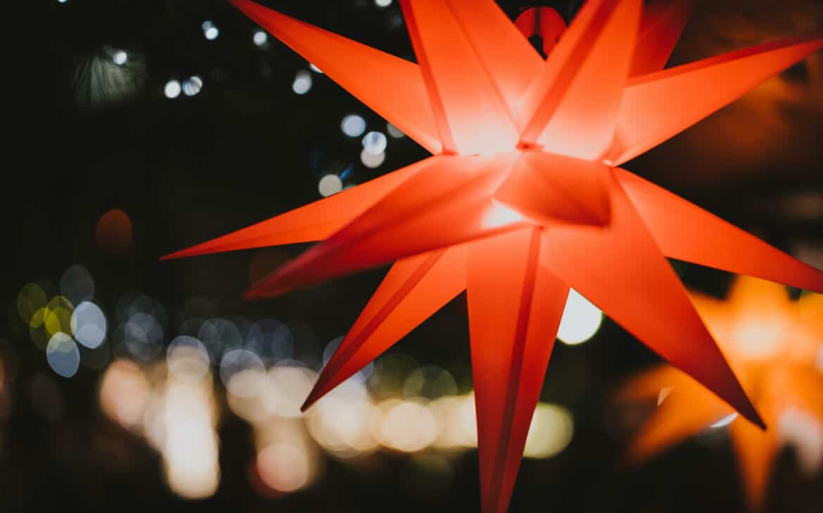 In einem Stand auf dem Weihnachtsmarkt hängt ein roter Faltstern, der von innen beleuchtet ist.