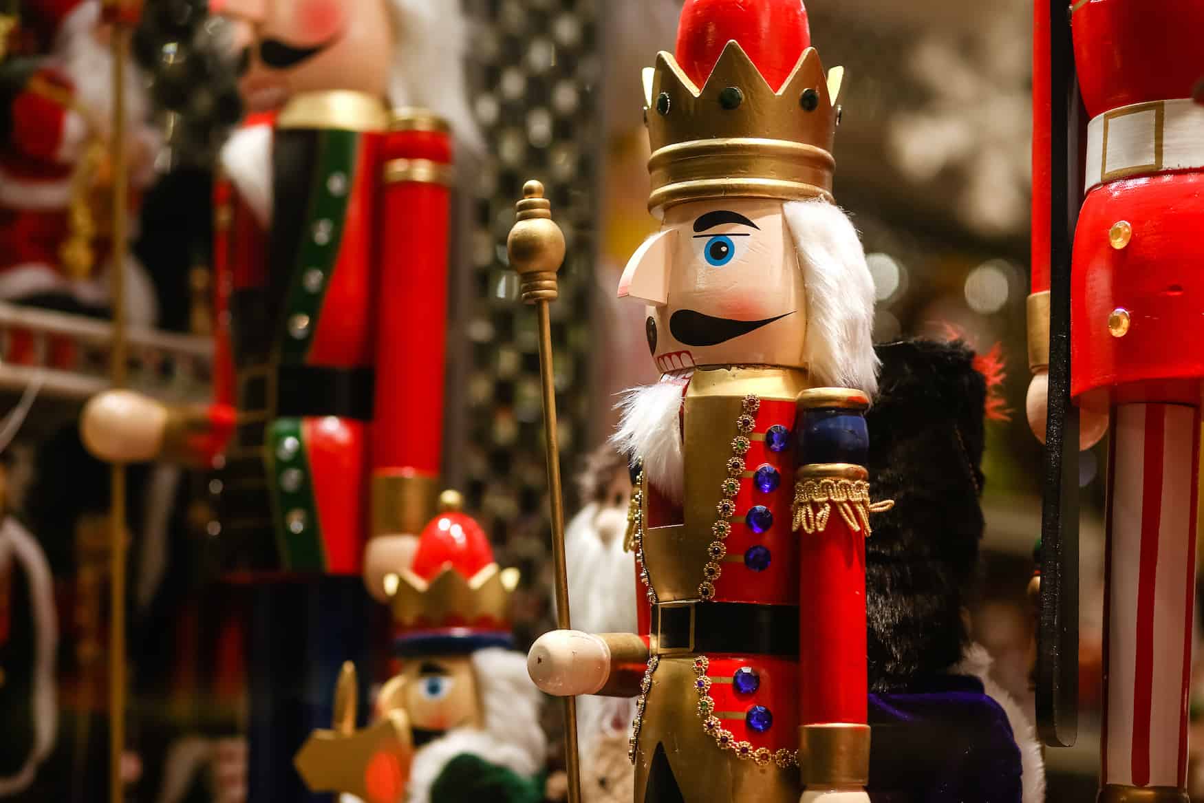 Ein Nussknacker-Soldat in roter Uniform und mit weißem Haar und Bart steht zwischen anderen Nussknackern in einer Hütte auf einem Weihnachtsmarkt.