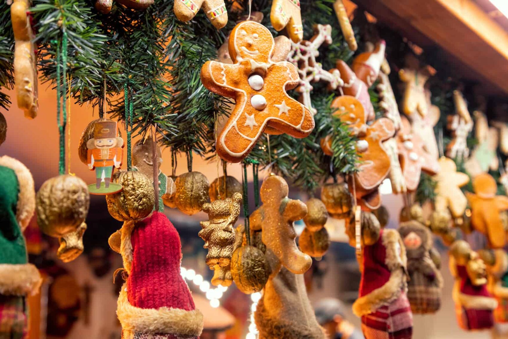 Eine Hütte auf dem Weihnachtsmarkt ist mit Tannenzweigen und Anhängern geschmückt. Ein Anhänger ist ein klassischer Lebkuchenmann in braun mit Verzierungen aus Zuckerguss.