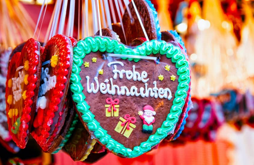 Ein mit Zuckerguss verziertes Lebkuchenherz mit dem Schriftzug "Frohe Weihnachten" hängt mit anderen Lebkuchenherzen in einem Stand auf dem Weihnachtsmarkt.