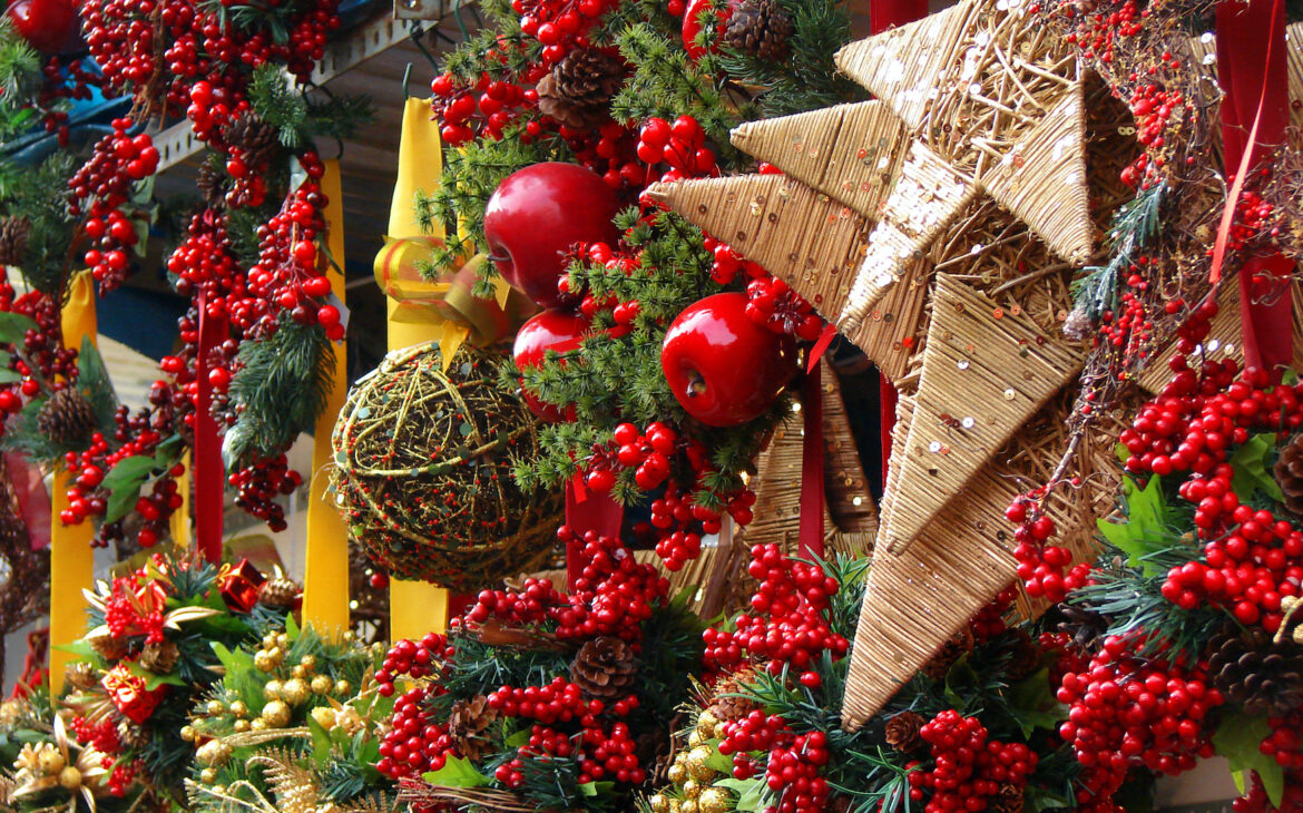 Ein Stand auf dem Weihnachtsmarkt ist festlich mit Sternen, Moos, roten Beeren und Äpfeln geschmückt.