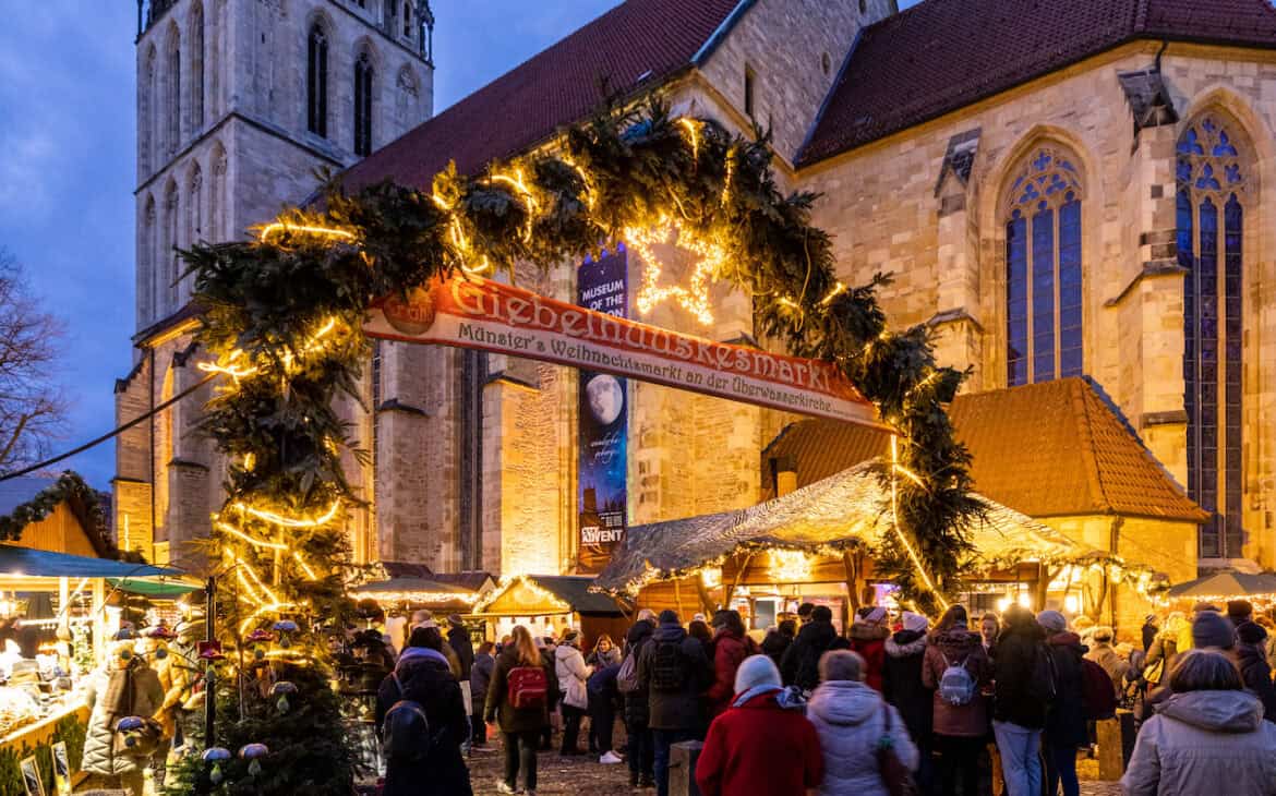 Der festlich geschmückte Eingangsbogen zum Giebelhüsskesmarkt and er Überwasserkirche mit vielen Menschen an den Ständen.