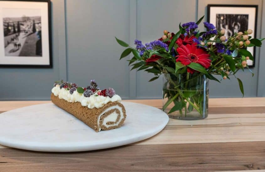 Dekorierte Gingerbread-Roulade auf Tisch angerichtet mit Blumenstrauß