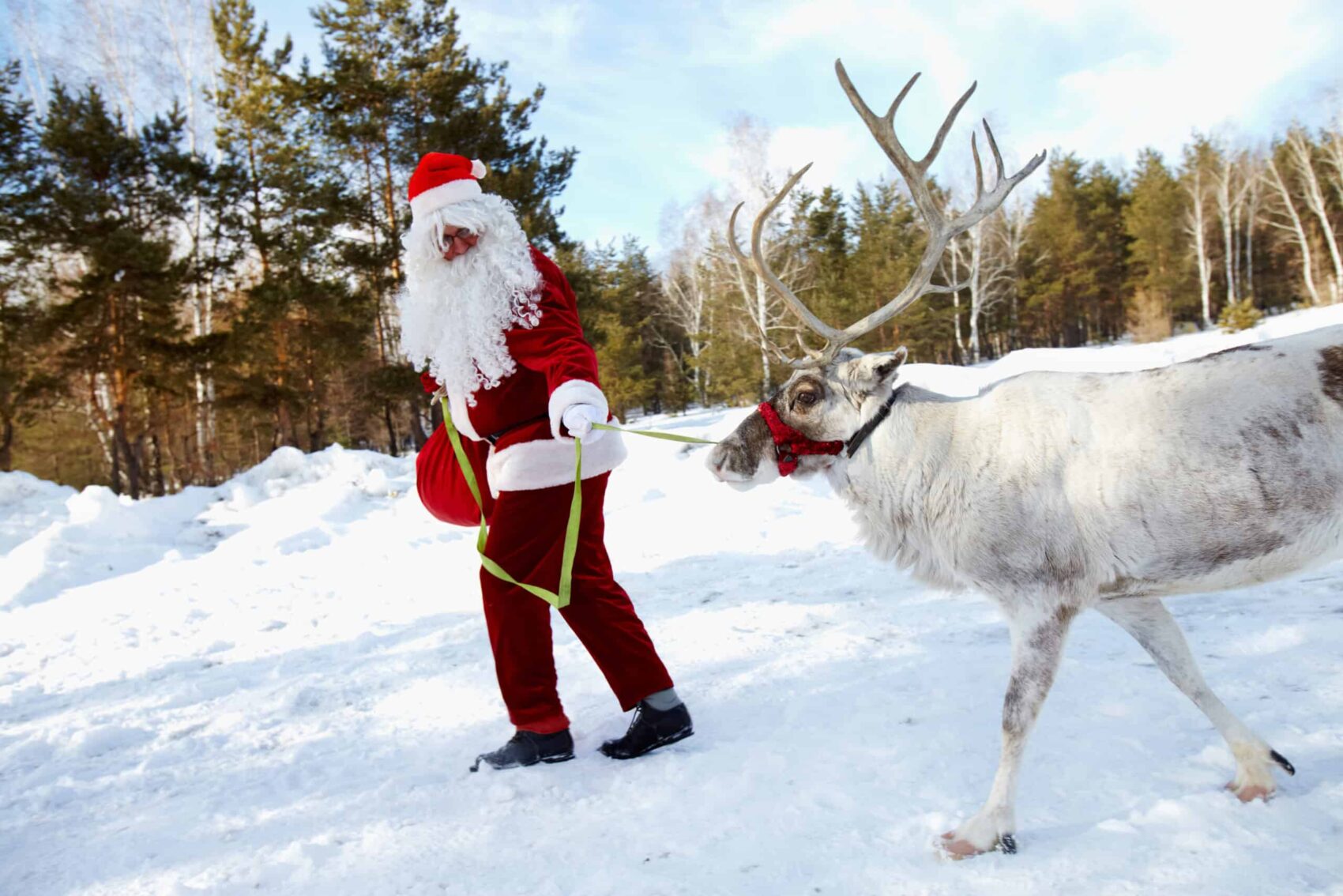 Weihnachtsmann führt Rentier an der Leine in Schneelandschaft