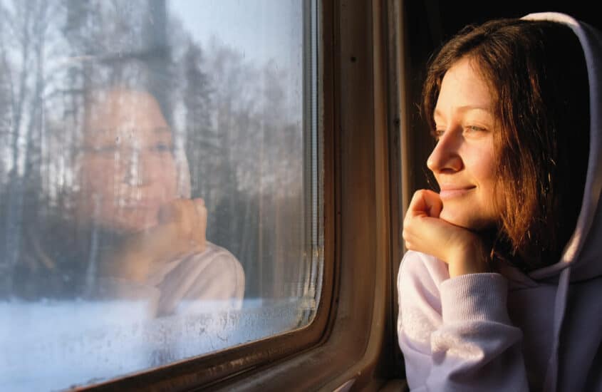 Mädchen im Zug guckt aus dem Fenster in eine winterliche Landschaft
