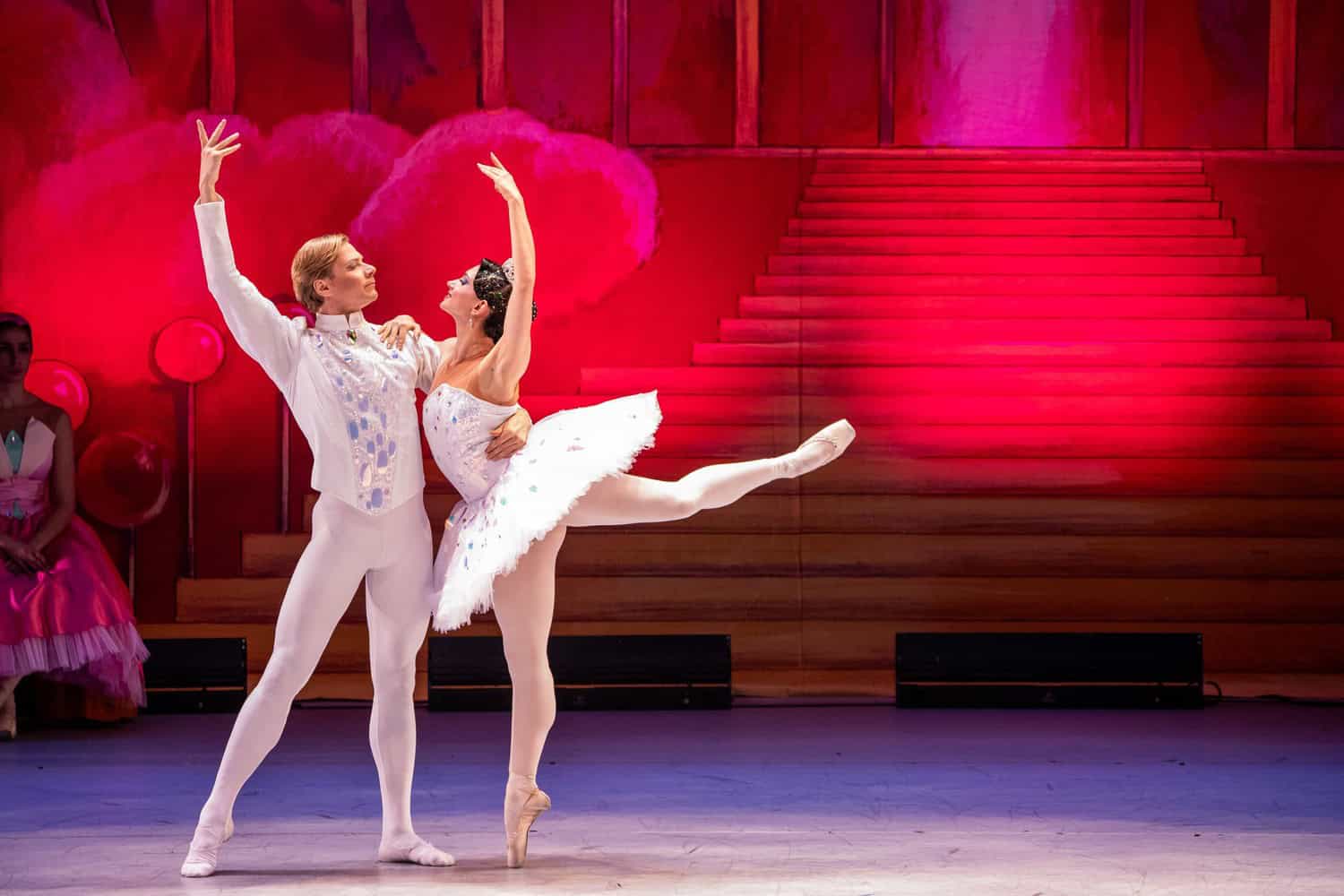 Tänzer und Tänzerin in weißen, glitzernden Kostümen im Nussknacker-Pas-de-deux vor einer rot beleuchteten Treppe