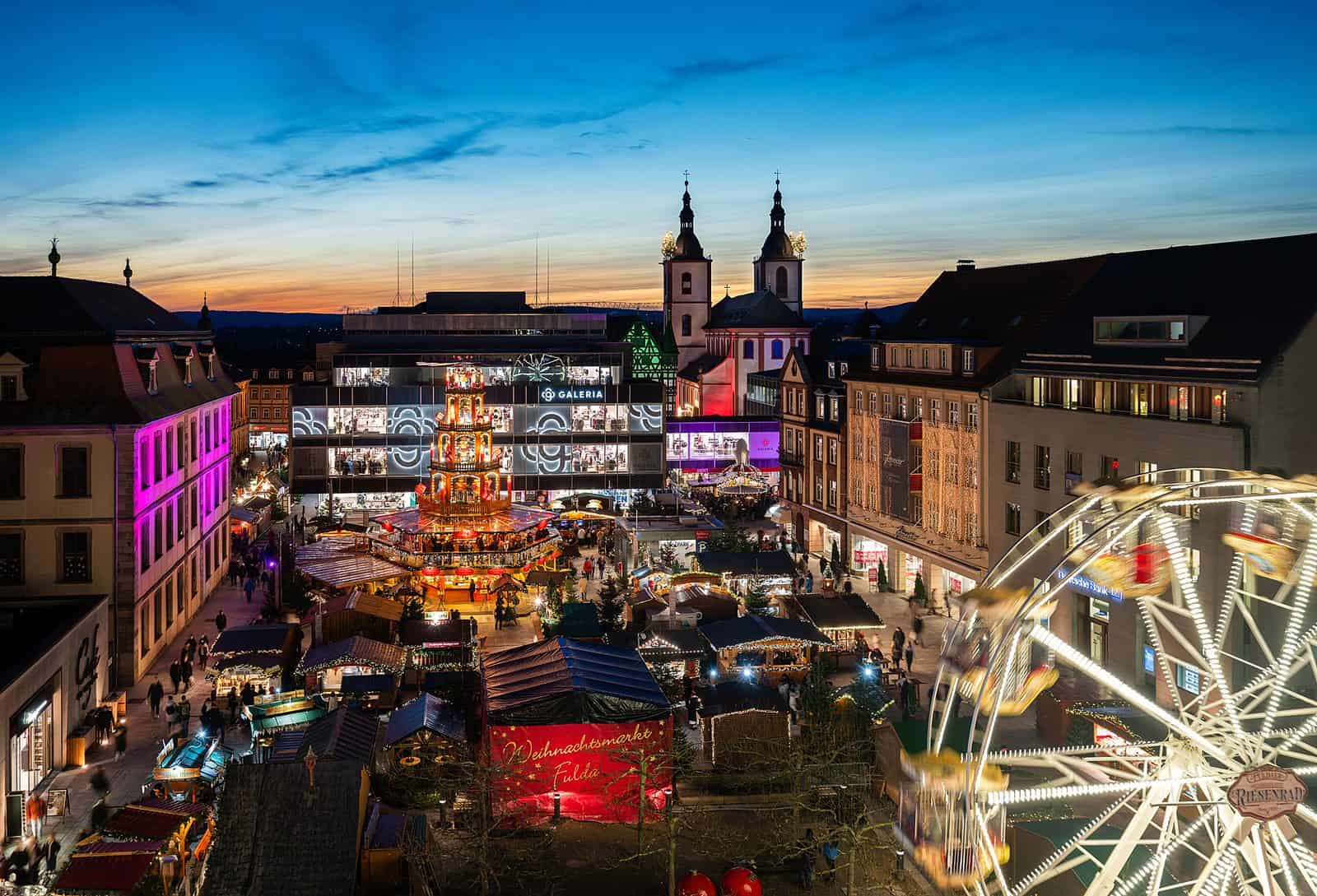 Weihnachtsmarkt Fulda von oben in der Abenddämmerung mit Weihnachtspyramide, Buden, Riesenrad und barocker Kirche