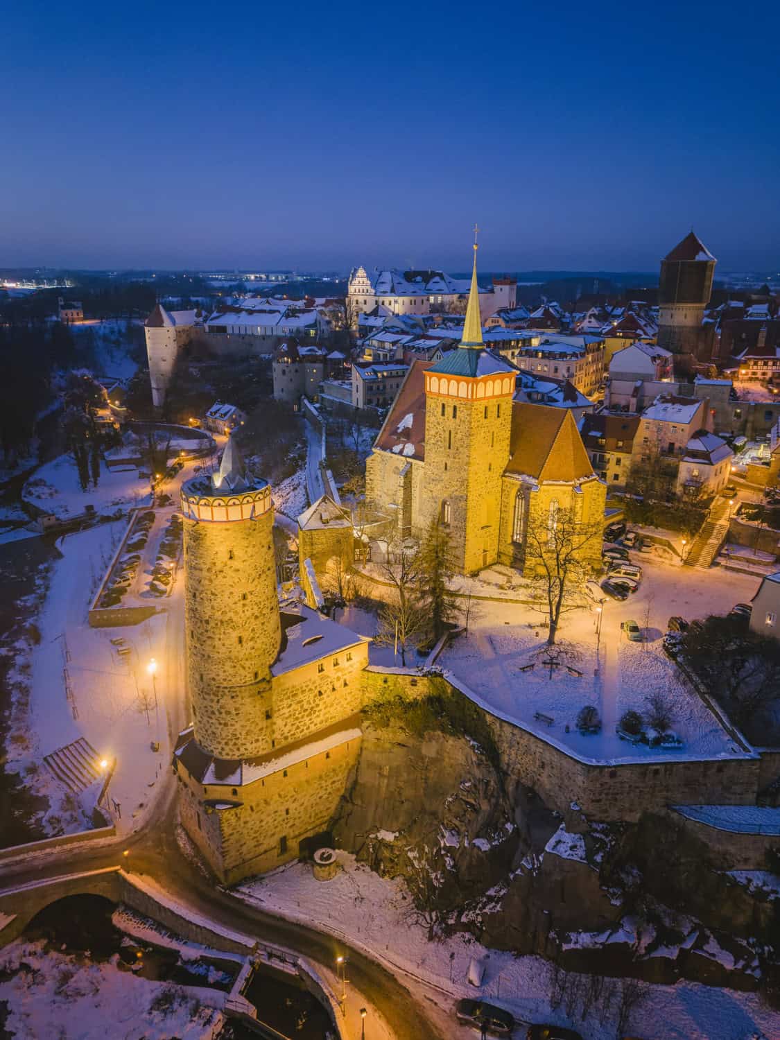 Beleuchtete Alte Wasserkunst und Michaeliskirche über der verschneiten Spree in Bautzen zur blauen Stunde