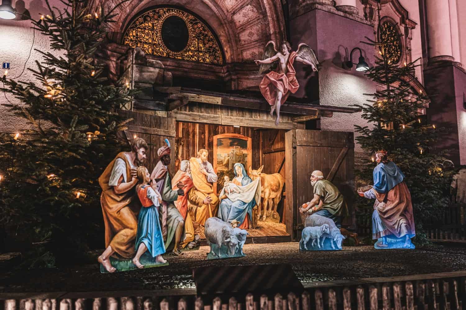Lebensgroße Weihnachtskrippe mit bemalten Holzfiguren vor einem Kirchenportal in Altötting.